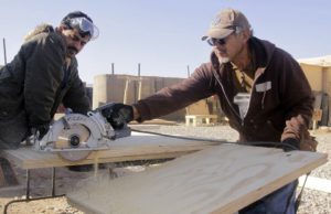 two men sawing a large bar with electric saw